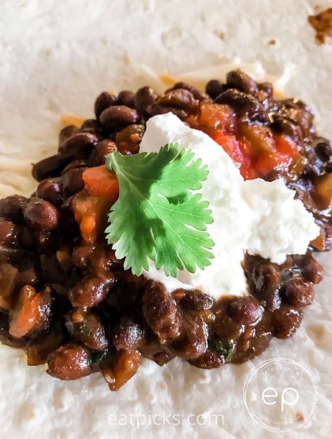 Black Beans with sour cream dollop and cilantro leaf on flour tortilla